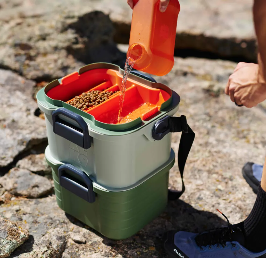 Pouring water and kibble into the open top tier of a stacked XLK9 Basecamp, with both tiers locked together underneath.